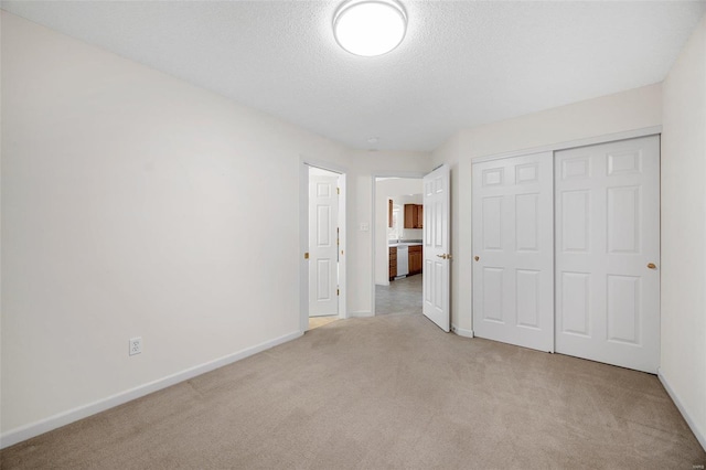 unfurnished bedroom with a closet, light colored carpet, a textured ceiling, and baseboards