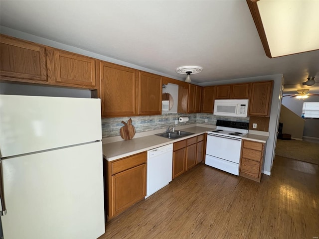 kitchen featuring tasteful backsplash, light countertops, wood finished floors, white appliances, and a sink