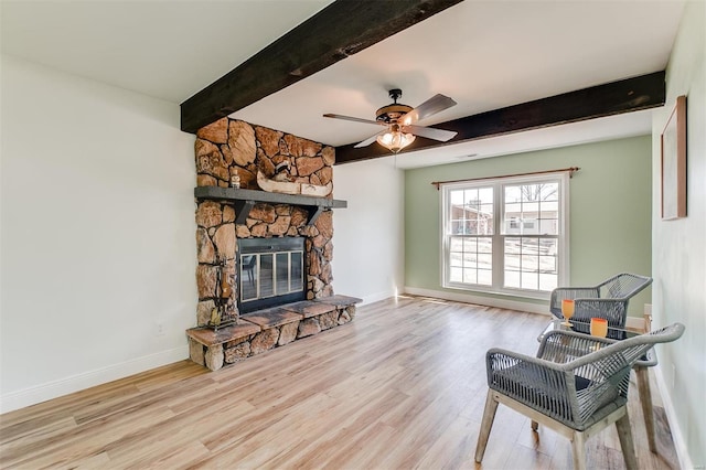 sitting room with wood finished floors, baseboards, beam ceiling, ceiling fan, and a stone fireplace