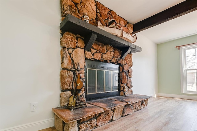 room details featuring beamed ceiling, a stone fireplace, baseboards, and wood finished floors