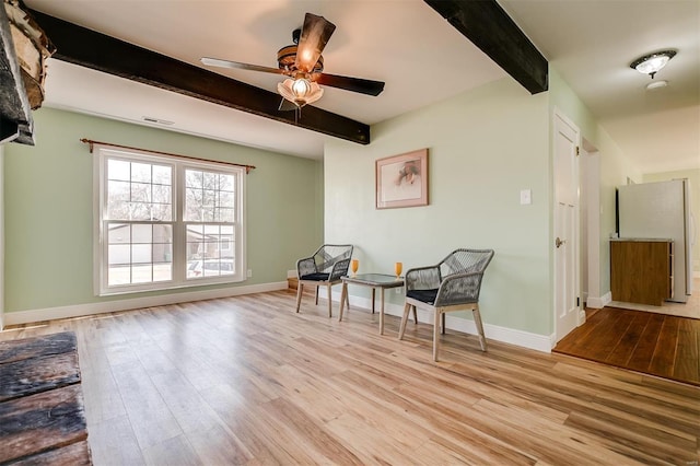 sitting room with beamed ceiling, visible vents, a ceiling fan, wood finished floors, and baseboards