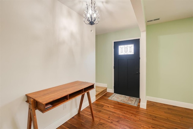 foyer entrance featuring a notable chandelier, wood finished floors, visible vents, and baseboards