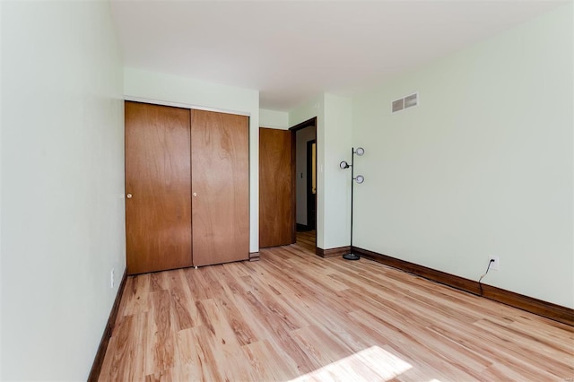 unfurnished bedroom with light wood-type flooring, visible vents, baseboards, and a closet