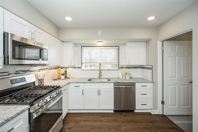 kitchen with a sink, light stone counters, white cabinetry, appliances with stainless steel finishes, and dark wood-style flooring