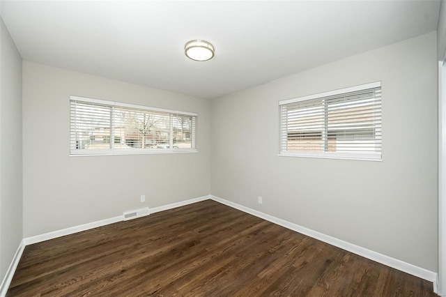 empty room with dark wood-style floors, visible vents, and baseboards