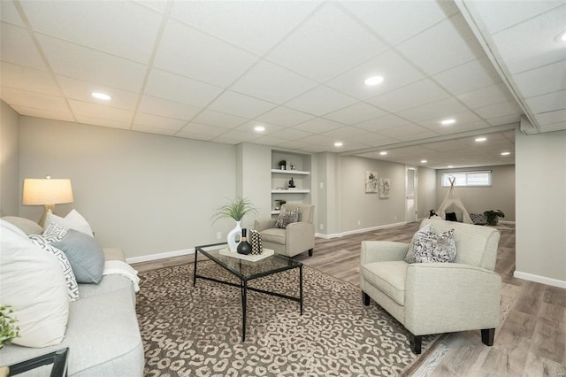 living area with built in shelves, wood finished floors, recessed lighting, baseboards, and a paneled ceiling