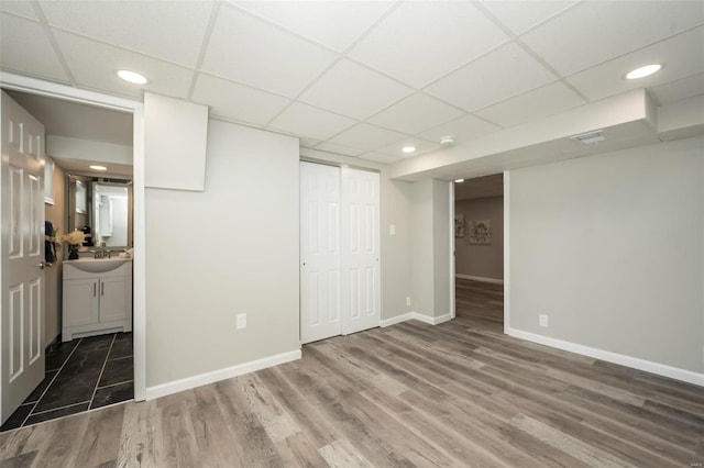 interior space with a sink, a paneled ceiling, baseboards, and wood finished floors