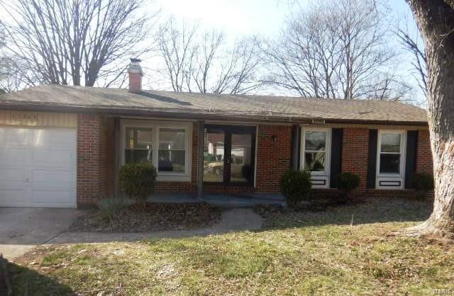 exterior space featuring covered porch, a chimney, a front lawn, a garage, and brick siding