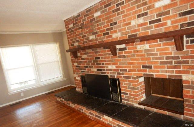 details featuring ornamental molding, a brick fireplace, baseboards, and wood finished floors