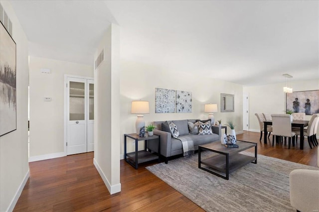 living room featuring visible vents, baseboards, wood finished floors, and a chandelier