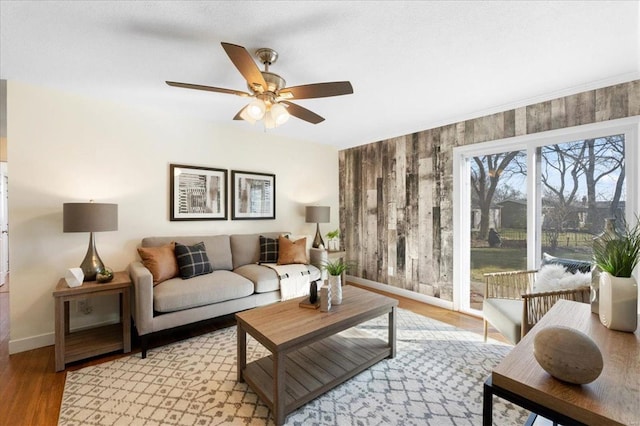 living area with a ceiling fan, light wood-type flooring, and baseboards