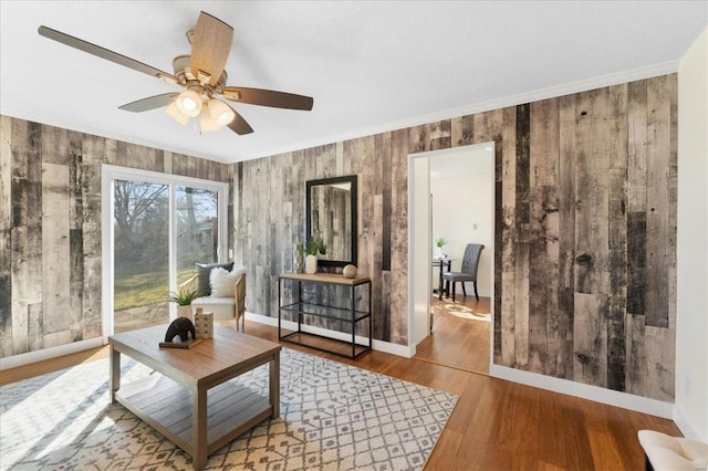 living room with ceiling fan, wood finished floors, baseboards, and ornamental molding