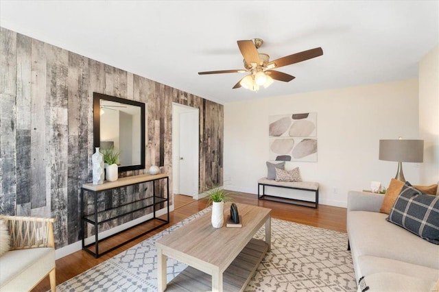 living room featuring wood finished floors, baseboards, wood walls, and ceiling fan