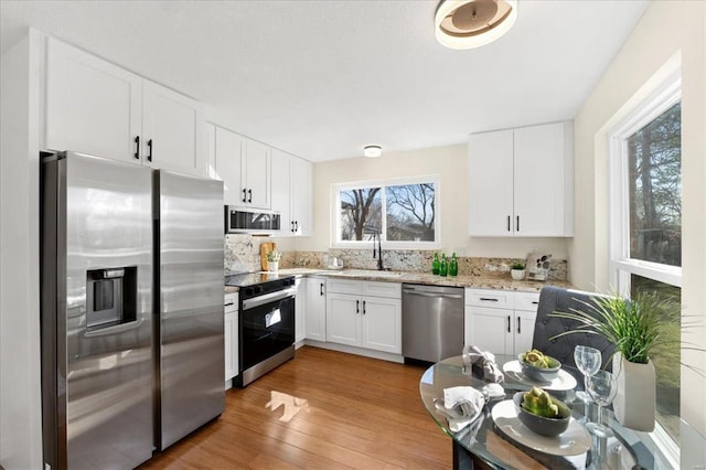 kitchen featuring light wood finished floors, light stone counters, white cabinets, stainless steel appliances, and a sink