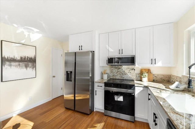 kitchen featuring light stone counters, appliances with stainless steel finishes, light wood-style floors, white cabinetry, and a sink