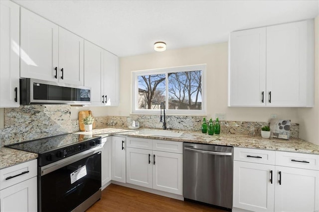 kitchen featuring light stone counters, white cabinetry, stainless steel appliances, and a sink