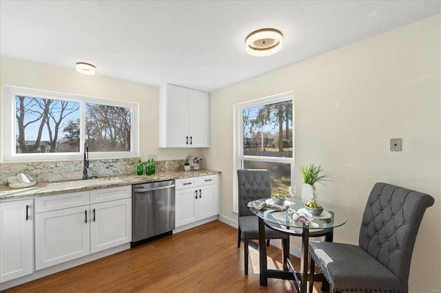 kitchen with stainless steel dishwasher, white cabinetry, light wood finished floors, and a sink