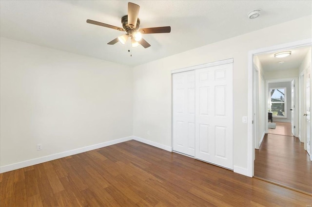 unfurnished bedroom with a closet, a ceiling fan, dark wood-type flooring, and baseboards