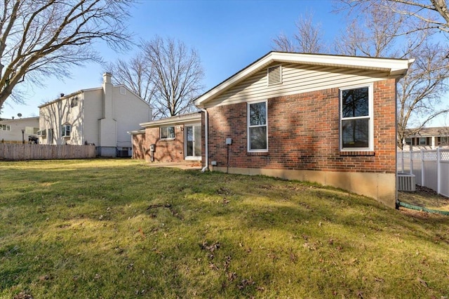 rear view of property with fence, brick siding, central AC, and a lawn