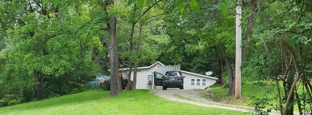 view of front facade featuring a wooded view, driveway, and a front yard