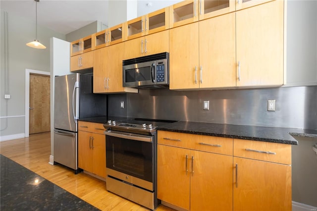 kitchen with light wood-style floors, stainless steel appliances, backsplash, and dark stone countertops