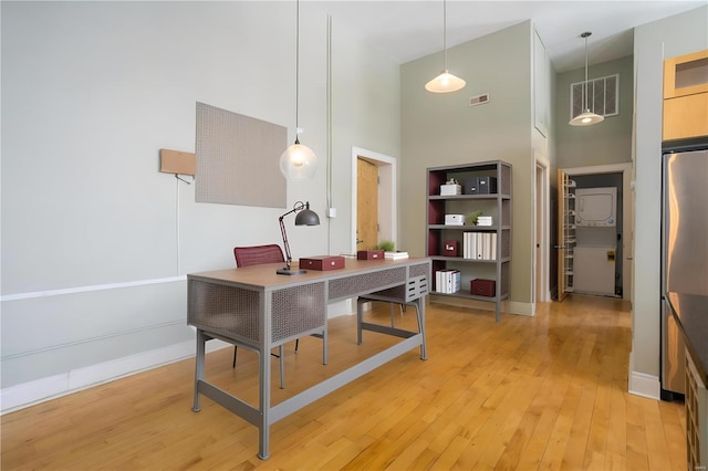 office space featuring a high ceiling, baseboards, visible vents, and light wood finished floors