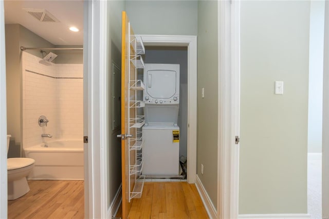 laundry area featuring wood finished floors, baseboards, visible vents, laundry area, and stacked washer and clothes dryer