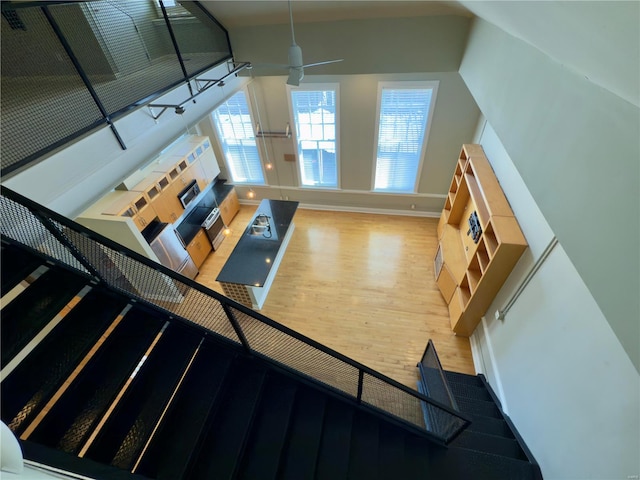 unfurnished living room with stairway, a ceiling fan, baseboards, and wood finished floors