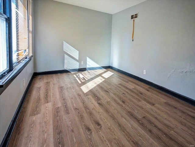 empty room featuring wood finished floors, visible vents, and baseboards