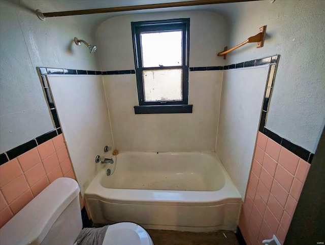 full bath featuring shower / bathtub combination, toilet, tile walls, and a textured wall