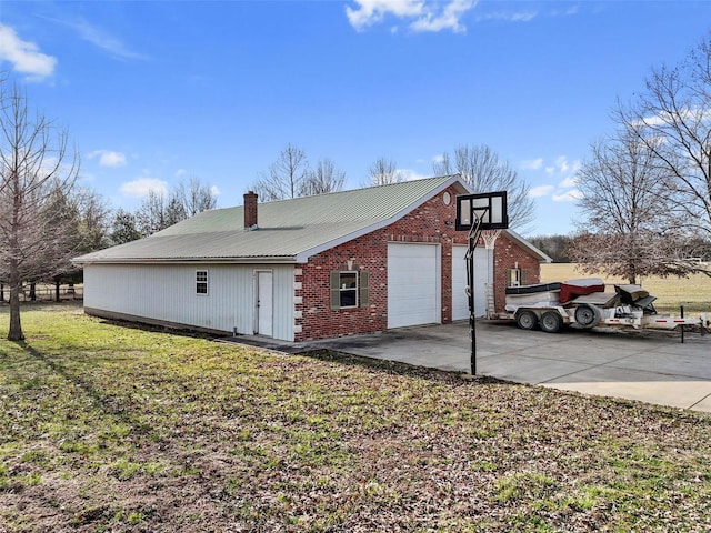 view of side of property featuring driveway, a yard, a chimney, a detached garage, and metal roof