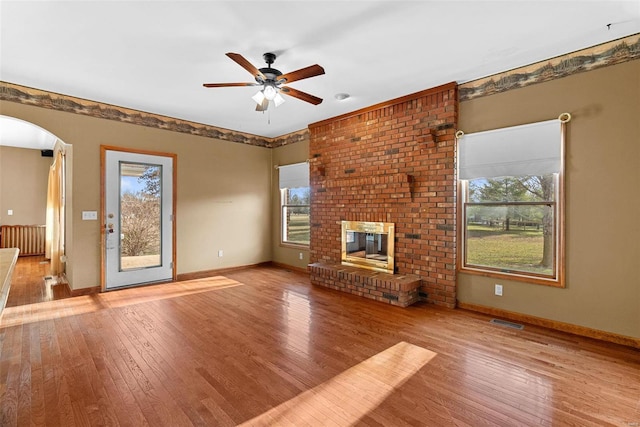 unfurnished living room with visible vents, a ceiling fan, hardwood / wood-style floors, arched walkways, and baseboards