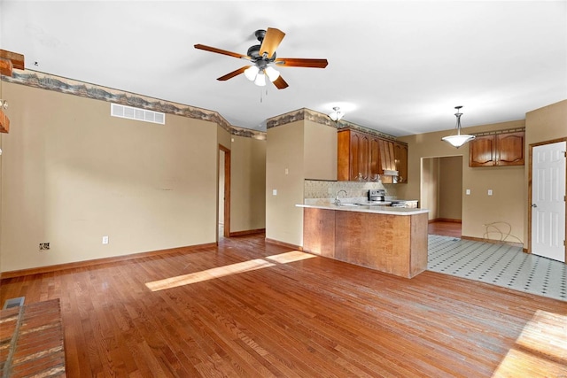 kitchen featuring a ceiling fan, visible vents, a peninsula, light countertops, and brown cabinets