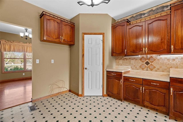 kitchen with brown cabinets, tasteful backsplash, an inviting chandelier, baseboards, and light floors