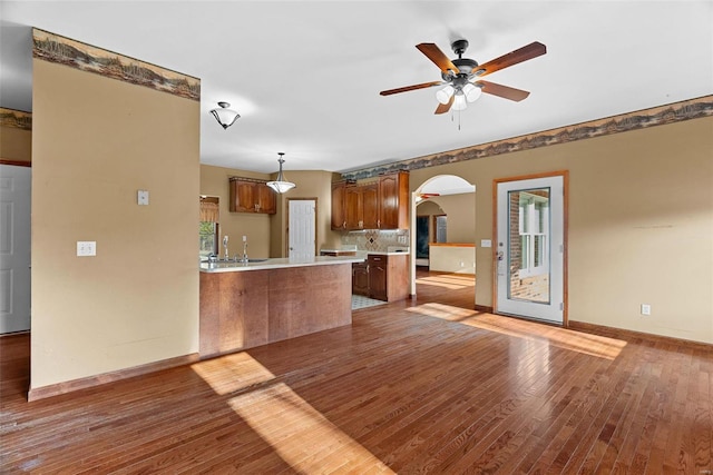 kitchen with hardwood / wood-style floors, a ceiling fan, a peninsula, arched walkways, and light countertops