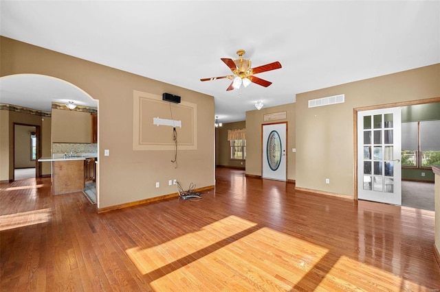 unfurnished living room with hardwood / wood-style floors, baseboards, visible vents, arched walkways, and ceiling fan