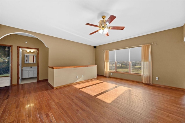 spare room featuring baseboards, wood-type flooring, arched walkways, and ceiling fan