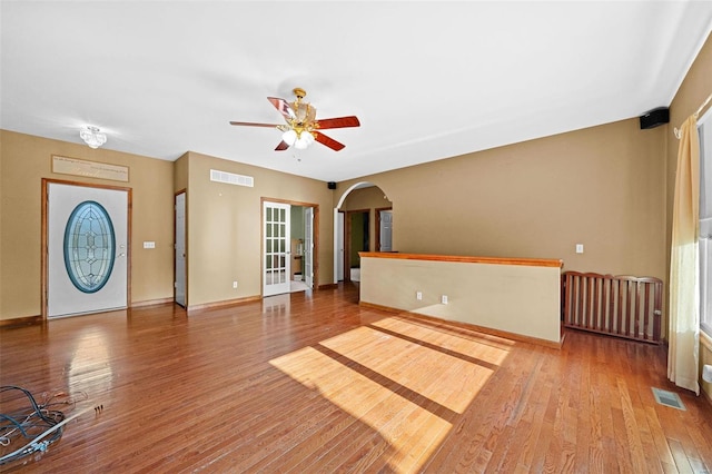 unfurnished living room with a ceiling fan, wood finished floors, visible vents, and arched walkways