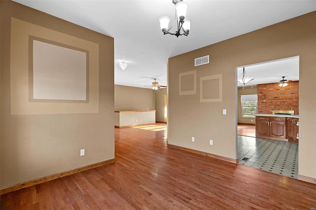 spare room featuring visible vents, ceiling fan with notable chandelier, baseboards, and wood finished floors