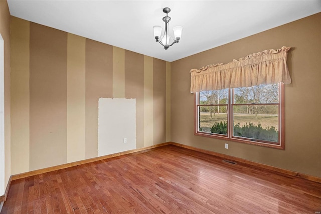 empty room featuring a notable chandelier, wood finished floors, visible vents, and baseboards