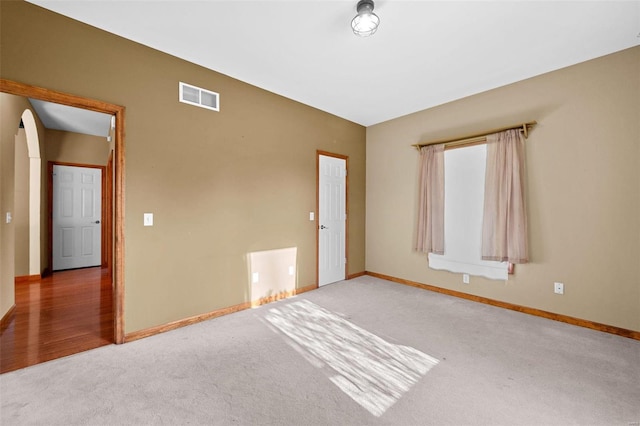 unfurnished room featuring arched walkways, visible vents, baseboards, and carpet floors