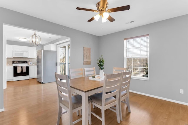 dining room featuring light wood-type flooring, visible vents, baseboards, and ceiling fan with notable chandelier