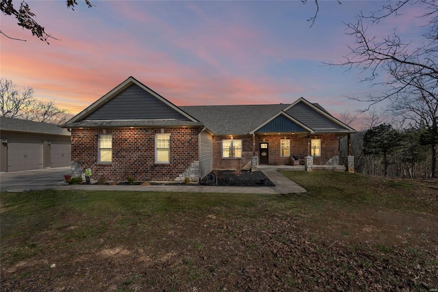 view of front of property with covered porch, a garage, a lawn, and brick siding