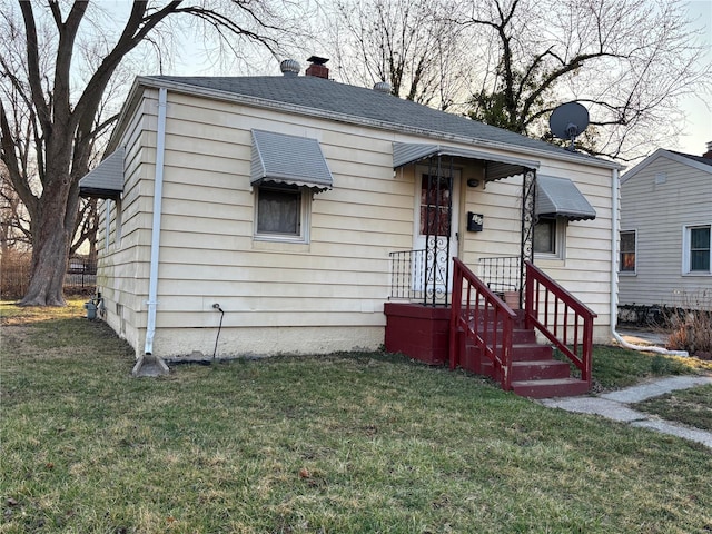 bungalow-style house with roof with shingles, a chimney, and a front lawn