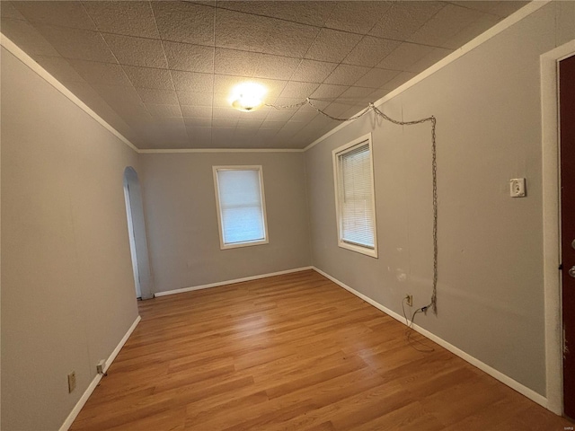 empty room with baseboards, arched walkways, light wood-style flooring, and crown molding