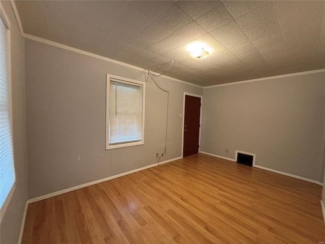 spare room with visible vents, baseboards, ornamental molding, and light wood finished floors