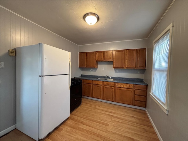 kitchen featuring black gas range oven, light wood-style flooring, freestanding refrigerator, dark countertops, and brown cabinets