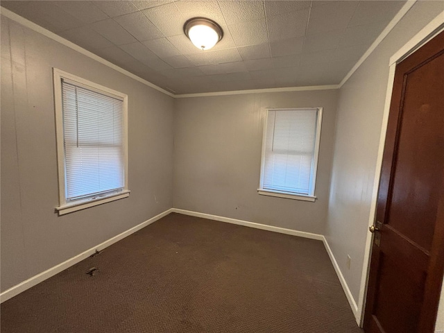 spare room featuring crown molding, baseboards, and dark colored carpet