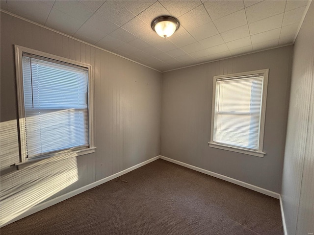 unfurnished room with ornamental molding, baseboards, and dark colored carpet