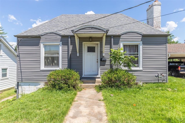 bungalow featuring a chimney, a shingled roof, and a front lawn